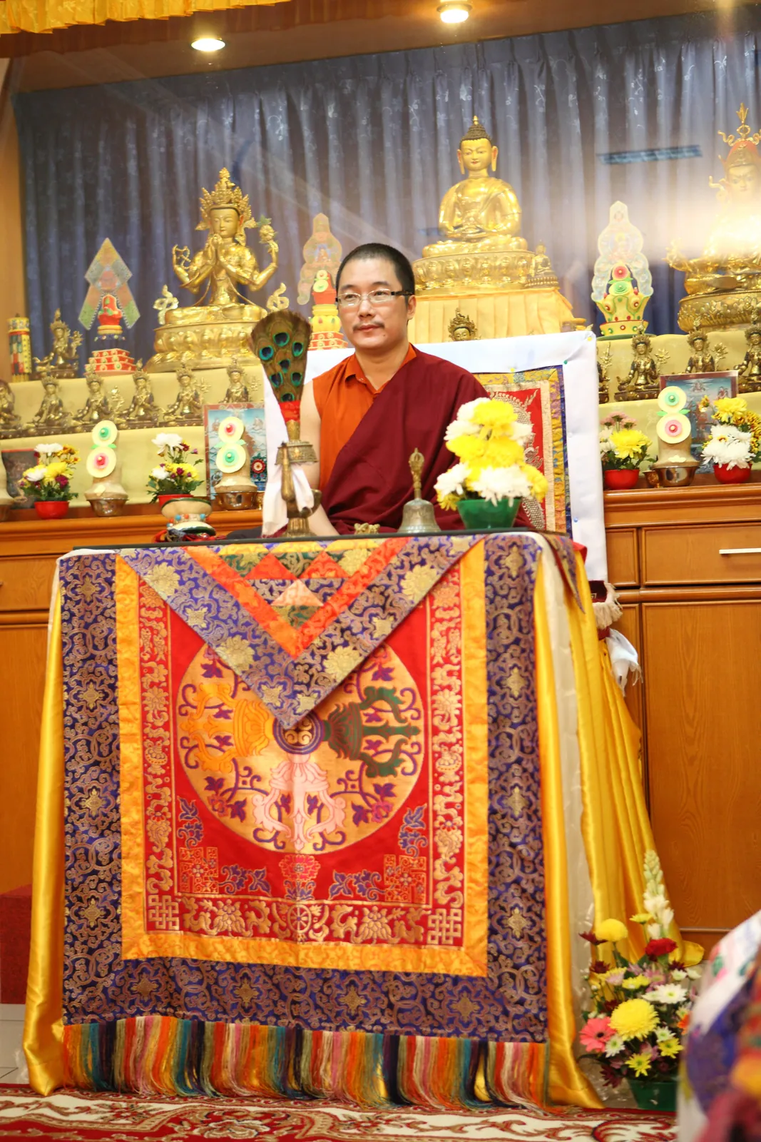 Yang Mulia Karma Kuchen Rinpoche di singgasana Dharma, dengan altar utama vihara di belakangnya.